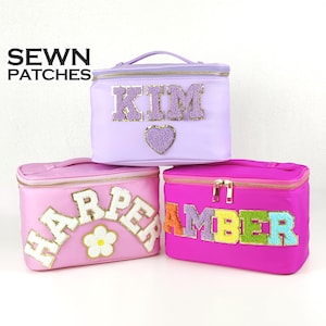 May include: Three cosmetic bags in shades of pink and purple, each with a different name embroidered on the front. The bags have a zippered closure and a top handle. The text "SEWN PATCHES" is in the upper left corner.