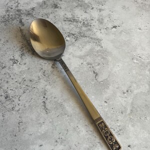 Puede incluir: Una cuchara de plata vintage con un cuenco ovalado y un mango largo. El mango presenta un diseño ornamentado cerca de la base y un patrón decorativo. La cuchara tiene un acabado pulido, que refleja la luz.
