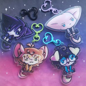 May include: A selection of anime-style cat character keyrings. Each keyring showcases a distinct cat design with varied colours and expressions. The keyrings have heart-shaped clasps in various colours, including black, green, and purple.