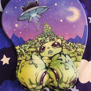 May include: A mouse mat with a quirky alien cat illustration. The design shows a purple and blue night sky with a crescent moon, stars, and a UFO. The foreground is packed with green alien cat characters. Text: etsy.com/shop/boycub.