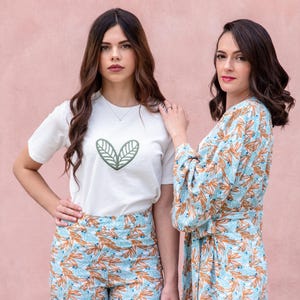 May include: Two women wearing matching outfits. One wears a white t-shirt with a green leaf design and patterned pants. The other wears a robe with a similar pattern. The outfits feature a light blue and orange leaf pattern.