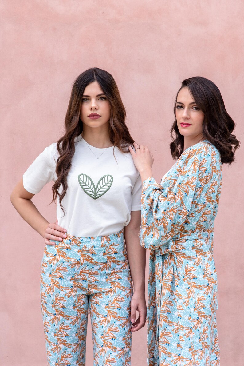 May include: Two women wearing matching outfits. One wears a white t-shirt with a green leaf design and patterned pants. The other wears a robe with a similar pattern. The outfits feature a light blue and orange leaf pattern.