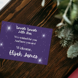 Op de afbeelding: Een paarse kaart met witte tekst en sterren die "Twinkle Twinkle Little Star We wished for you And here you are! Welcome, Elijah James" zegt.