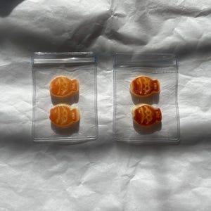May include: Two clear plastic bags each containing two orange fish-shaped gummies. The gummies are in a clear plastic bag with a white background.