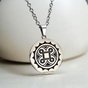 May include: A silver-colored pendant necklace with a circular pendant. The pendant features a black and white geometric design within a scalloped border. The necklace chain is also silver-colored.