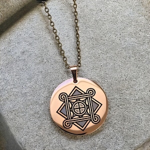 May include: A circular rose gold pendant necklace featuring a dark engraved geometric design. The pendant displays a central cross within a circle, surrounded by a square frame with curled corners and a star-shaped background. It hangs from a thin bronze chain.