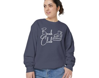 Puede incluir: Una sudadera azul marino con el texto "Book Club" en letras blancas en cursiva. Un contorno blanco de una taza y una pila de libros está al lado del texto.