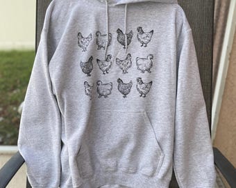 Puede incluir: Una sudadera con capucha gris con un estampado negro de varios pollos en la parte delantera.