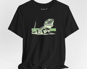 Op de afbeelding: Zwart t-shirt met een lichtgroene illustratie van een baardagaam. Het ontwerp bevat horizontale strepen en de tekst "My Shoe h" rechtsboven.