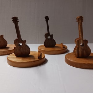 May include: Four wooden guitar stands with guitar shaped cutouts. The stands are made of light brown wood and the guitar cutouts are made of dark brown wood.