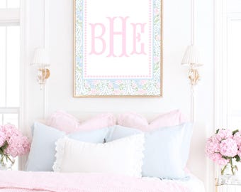 May include: A rectangular wall art print in a gold frame featuring the letters BHE in a large pink serif font. The print has a white center bordered by a light blue and pink floral pattern with a small pink dot trim around the monogram.