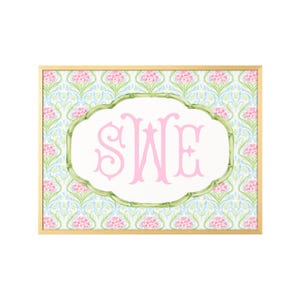 May include: A rectangular wall art print in a gold frame featuring a repeating pattern of pink hydrangea flowers and light blue foliage. In the center, a white scalloped frame with a green bamboo-style border displays the pink monogram letters SWE.