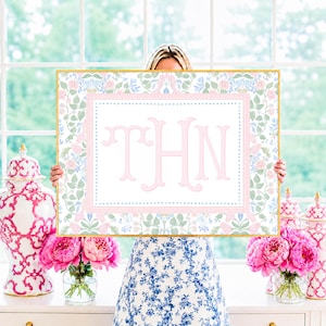 May include: A rectangular framed print featuring a central white panel with the pink monogram letters THN, surrounded by a border of pink and blue floral patterns on a white background, encased in a thin gold frame with a clean aesthetic.