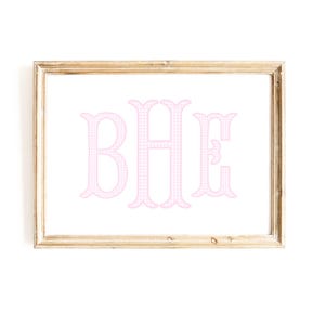 May include: A rectangular wooden frame containing a white print with the large pink monogram letters BHE. The letters feature a subtle white grid pattern throughout their design. The frame has a natural light brown wood grain finish.