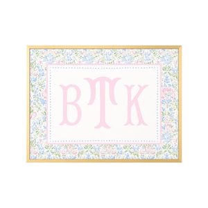 May include: A rectangular wall art piece in a gold frame featuring a central white panel with the light pink monogram letters BTK. The panel is bordered by a light pink dotted line and surrounded by a floral pattern in shades of blue and pink.