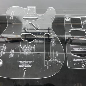 Könnte beinhalten: Ein Set aus transparenten Acryl-Frässchablonen für T-Style-Gitarren mit aufgedruckten technischen Spezifikationen, darunter eine Breite von 32,4 cm, eine Korpusdicke von 4,45 cm sowie Maße für Steg, Tonabnehmer und die Ausgangsbuchse.