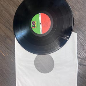 Puede incluir: Un disco de vinilo negro con una etiqueta roja y verde, sobre una funda de papel blanca. El disco tiene surcos conc&eacute;ntricos y la etiqueta dice "ONE" y "STEREO". El logotipo de Atlantic Records es visible.