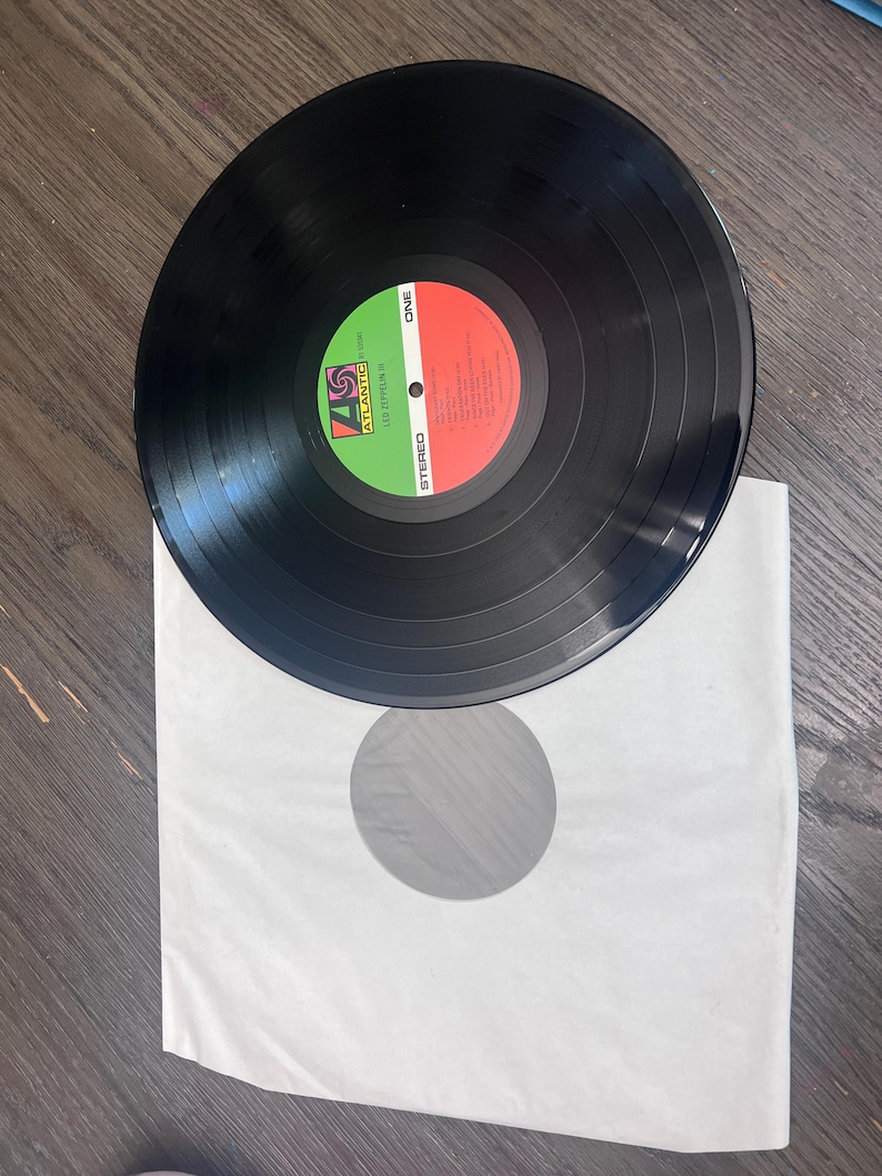 Puede incluir: Un disco de vinilo negro con una etiqueta roja y verde, sobre una funda de papel blanca. El disco tiene surcos conc&eacute;ntricos y la etiqueta dice "ONE" y "STEREO". El logotipo de Atlantic Records es visible.