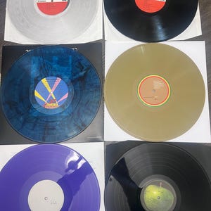 Puede incluir: Una colecci&oacute;n de seis discos de vinilo en varios colores, incluyendo transparente, negro, azul, dorado y morado. Cada disco est&aacute; en una funda de papel blanco. Las etiquetas de los discos presentan dise&ntilde;os y texto coloridos.