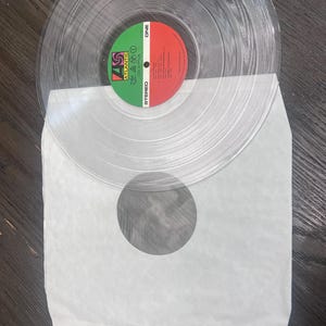 Puede incluir: Un disco de vinilo transparente con una etiqueta verde y roja, con el logotipo de Atlantic Records y el texto "Led Zeppelin". El disco est&aacute; en una funda de papel blanco. El vinilo transparente permite ver el disco.