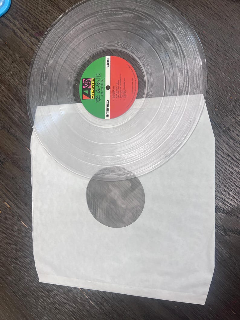 Puede incluir: Un disco de vinilo transparente con una etiqueta verde y roja, con el logotipo de Atlantic Records y el texto "Led Zeppelin". El disco est&aacute; en una funda de papel blanco. El vinilo transparente permite ver el disco.