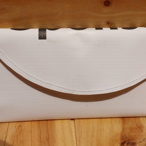 May include: White envelope clutch with a flap closure. The clutch is made of a smooth, white material and has a subtle sheen.