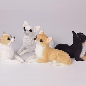 May include: Four Chihuahua dog ornaments in white, tan, and black. The dogs are depicted in a relaxed, lying-down position, with their heads raised. The ornaments are detailed and appear to be made of a smooth material.