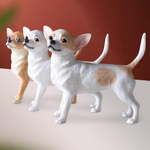 Könnte beinhalten: Drei Chihuahua-Figuren. Die erste ist hellbraun, die zweite weiß und die dritte weiß mit braunen Flecken. Alle haben aufrechte Ohren und stehen.