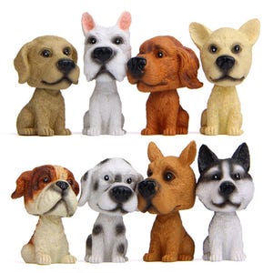 May include: Eight dog figurines with bobbleheads in various colours. The dogs are in different breeds, including tan, white, brown, and black. Each figurine is sitting upright with detailed facial features. The collection is on a white background.