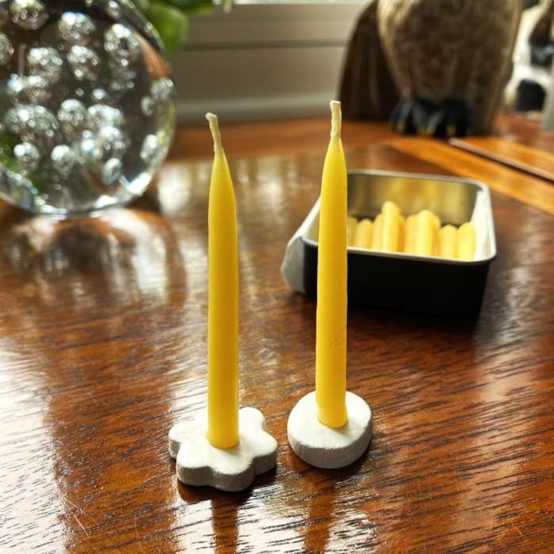 Two 20 minute candles standing in simple candle holders on a wooden table, with an open tin of beeswax Relaxation Candles behind them.