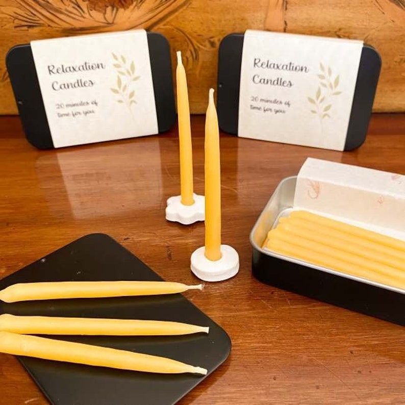 Two mini taper candles standing in ceramic holders, with three tins of beeswax 20 minute candles arranged around them