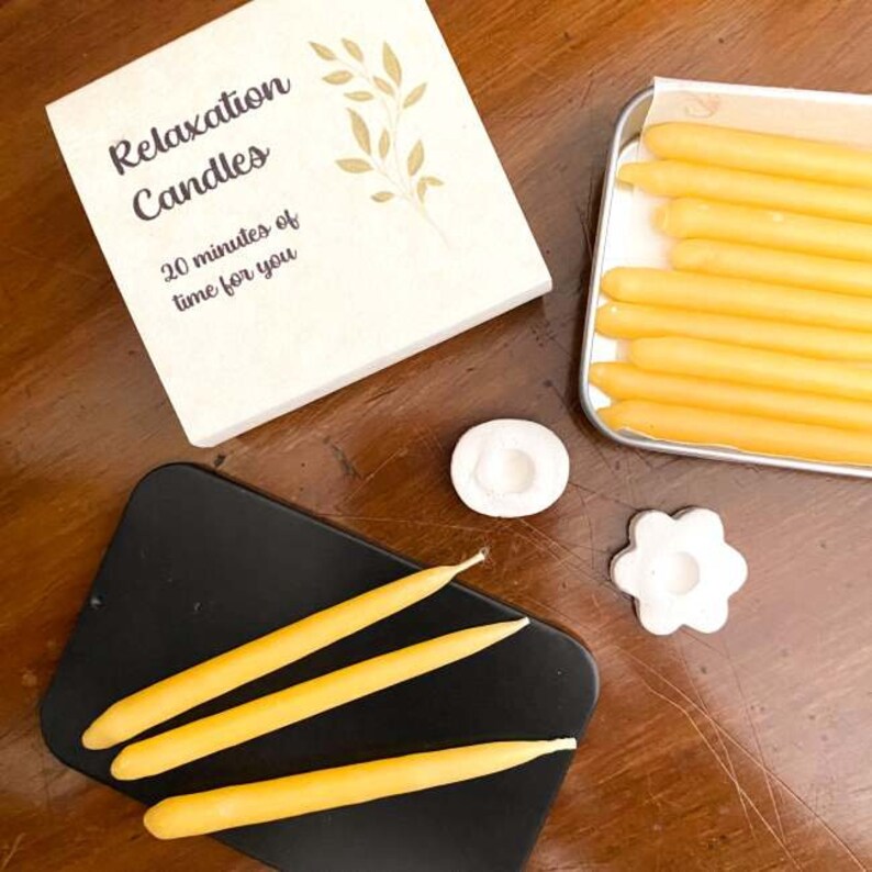 Three beeswax relaxation candles arranged on the lid of their black storage tin, with a stack of more 20 minute candles on one side.