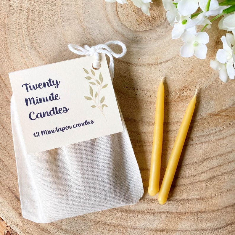 Cotton bag containing 12 twenty-minute candles, with two pure beeswax mini taper candles lying next to it, on a wooden table.