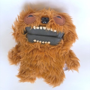 May include: A plush toy in the shape of a furry, brown creature with large, white teeth and a gray mouth. The toy has brown eyes and a black nose. The toy is made of soft, fuzzy material.