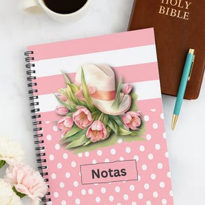 May include: A spiral-bound notebook with a pink polka dot and striped cover, featuring a floral and hat illustration. The word "Notas" is displayed on the cover. A cup of coffee, a Bible, and a pen are also visible.