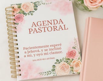 May include: A spiral-bound "AGENDA PASTORAL" notebook with gold-colored binding, featuring floral illustrations and text in Spanish. A pair of peach-colored glasses and a matching book are next to it. A vase of peach roses is in the background.