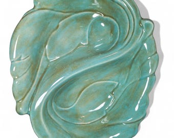 May include: A teal-colored ceramic leaf-shaped dish. The dish has a glossy finish and a detailed leaf vein design. The edges of the dish are slightly raised, and the overall shape is oval. The color is a mix of teal and brown.