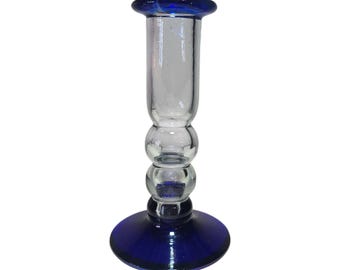 May include: A blue glass candle holder with a clear glass center and a round base. The holder has three decorative glass balls in the center.