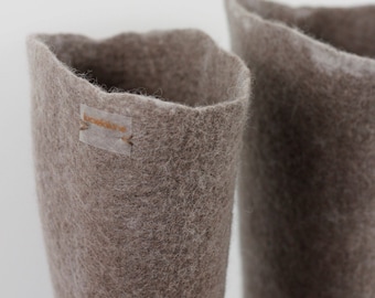 Puede incluir: Un par de botas altas de lana afieltrada de color marrón claro con una superficie texturizada y fibrosa. Una pequeña etiqueta rectangular de tela semitransparente con el texto "lucielune" en letras marrones está cosida en el lado izquierdo.