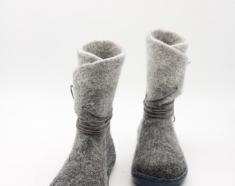 Puede incluir: Un par de botas de fieltro gris con suela gris oscuro y un cordón de cuero gris. Las botas tienen la parte superior doblada.