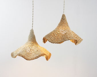 May include: Two pendant lights with a woven, natural fiber shade. The shades have a flared, bell-like shape and hang from a neutral-colored cord. The lights are illuminated, casting a warm glow.