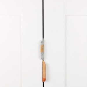 May include: Two cabinet door pulls, one gray and one orange, are mounted on a white door.