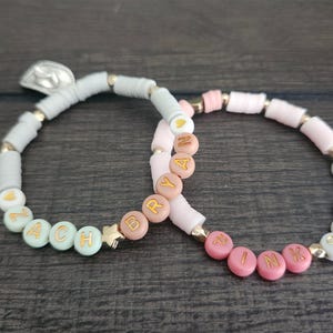 May include: Two beaded bracelets with the names "ZACH" and "BRYAN" spelled out in gold letters on pastel colored beads.