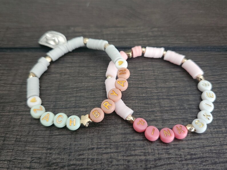 May include: Two beaded bracelets with the names "ZACH" and "BRYAN" spelled out in gold letters on pastel colored beads.