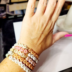 May include: A stack of colorful beaded bracelets with gold letter beads spelling out the words "SMOKESHOP", "OKLAHOMA", "GOOD", "PINK", "BRYANT", "SPREE", and "EACH".