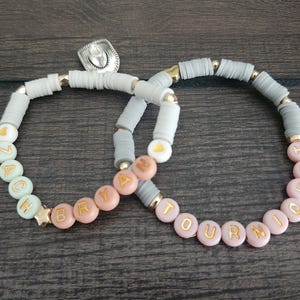 May include: Two beaded bracelets with the names "Zach" and "Bryah" on one and "Tourniquet" on the other. The bracelets are made with gray, pink, and green beads.