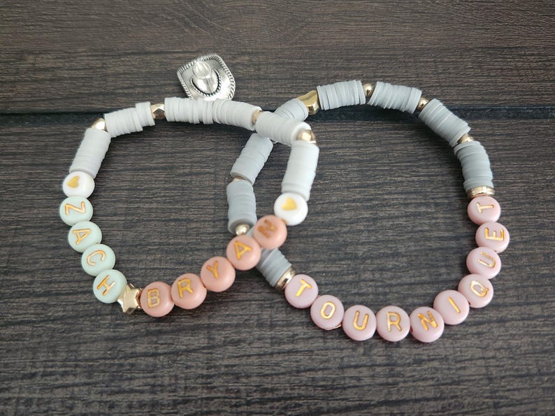 May include: Two beaded bracelets with the names "Zach" and "Bryah" on one and "Tourniquet" on the other. The bracelets are made with gray, pink, and green beads.