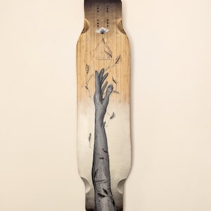 May include: A longboard deck with a hand reaching up towards a white flower. The hand is painted in shades of gray and black, and the flower is surrounded by delicate black vines. The background is a gradient of brown and white.