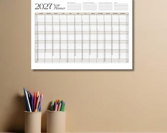 Puede incluir: Un calendario de pared 2027 blanco con un diseño de cuadrícula que muestra los meses de enero a diciembre, días numerados y cuatro secciones de notas en blanco en la parte superior, situado sobre dos portalápices.