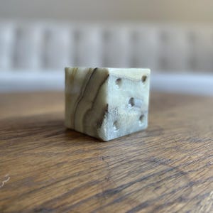 Peut inclure: Un dé en marbre blanc et vert avec six faces et des points noirs. Le dé est posé sur une surface en bois.